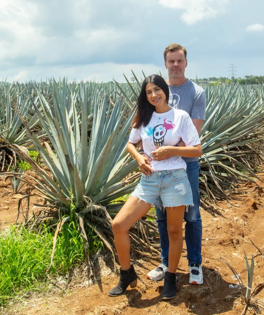 Founder HP hugging his wife Adriana from behind while standing inside an agave field.