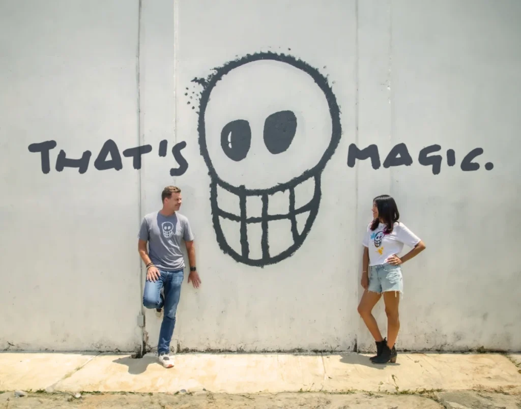 Founder HP and his wife Adriana standing in front of a white wall looking at each other. Inbetween of them is a huge black skull. Next to it it is written "That's magic."