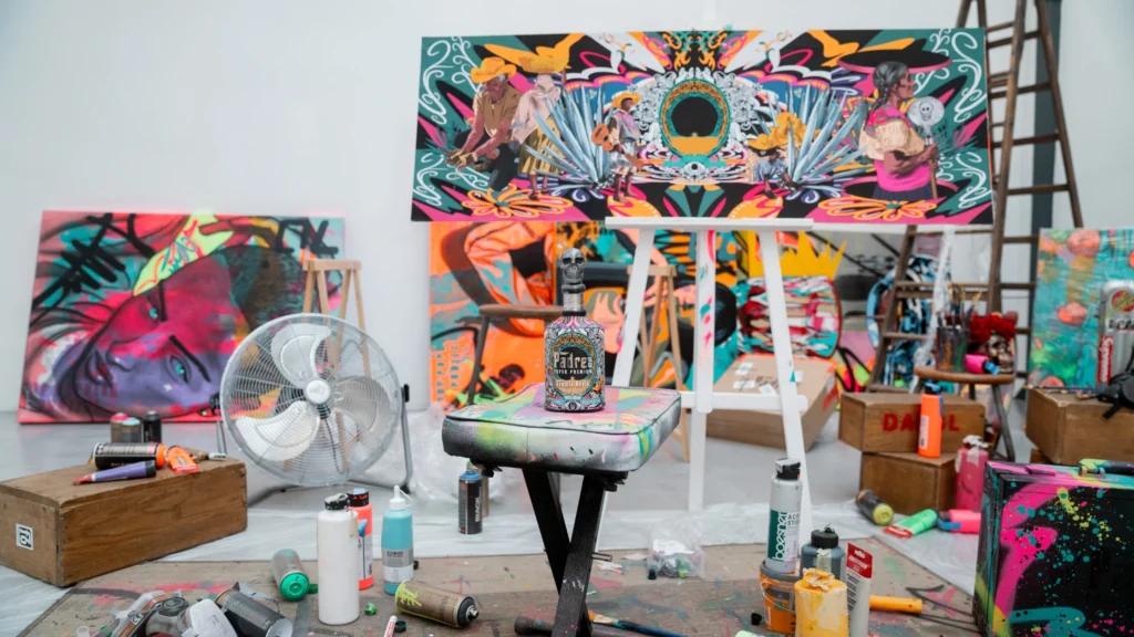 The new artist edition of Padre Azul in cooperation with artist Luis Morales. The bottle stands on a foldable chair used for painting. In the background there are colorful paintings, color tubes and bruches.