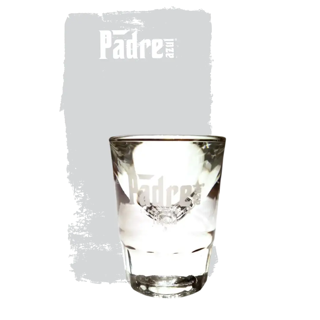 Padre Azul Shot Glass in front of a gray background. It has a solid base, gets wider towards the top. A white Padre Azul logo is place in the center.